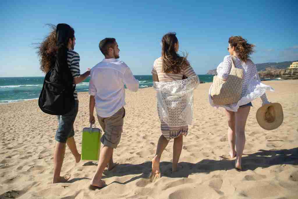 four friends on a beach carrying a cooler