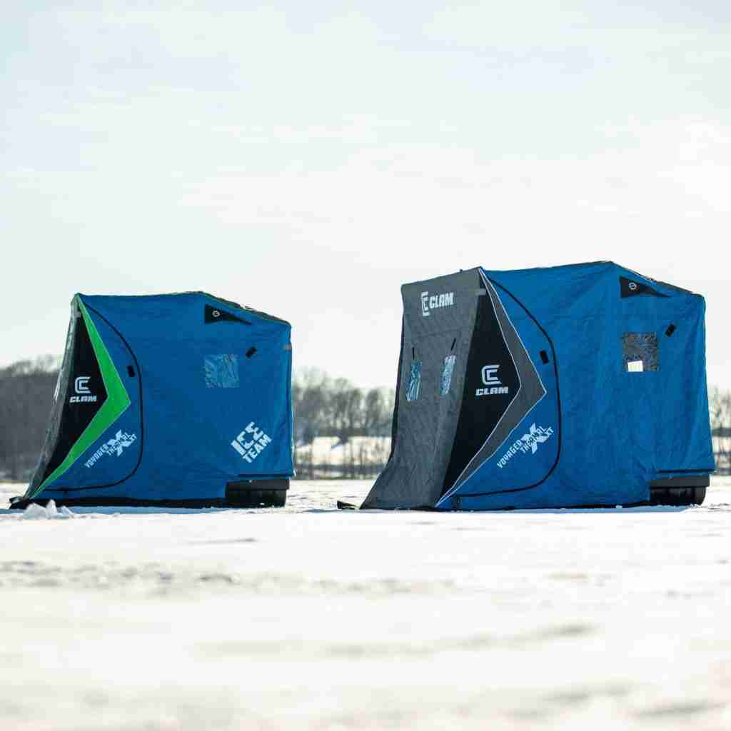 Blue cube-shaped ice shelters for ice fishing on snow-covered ice.