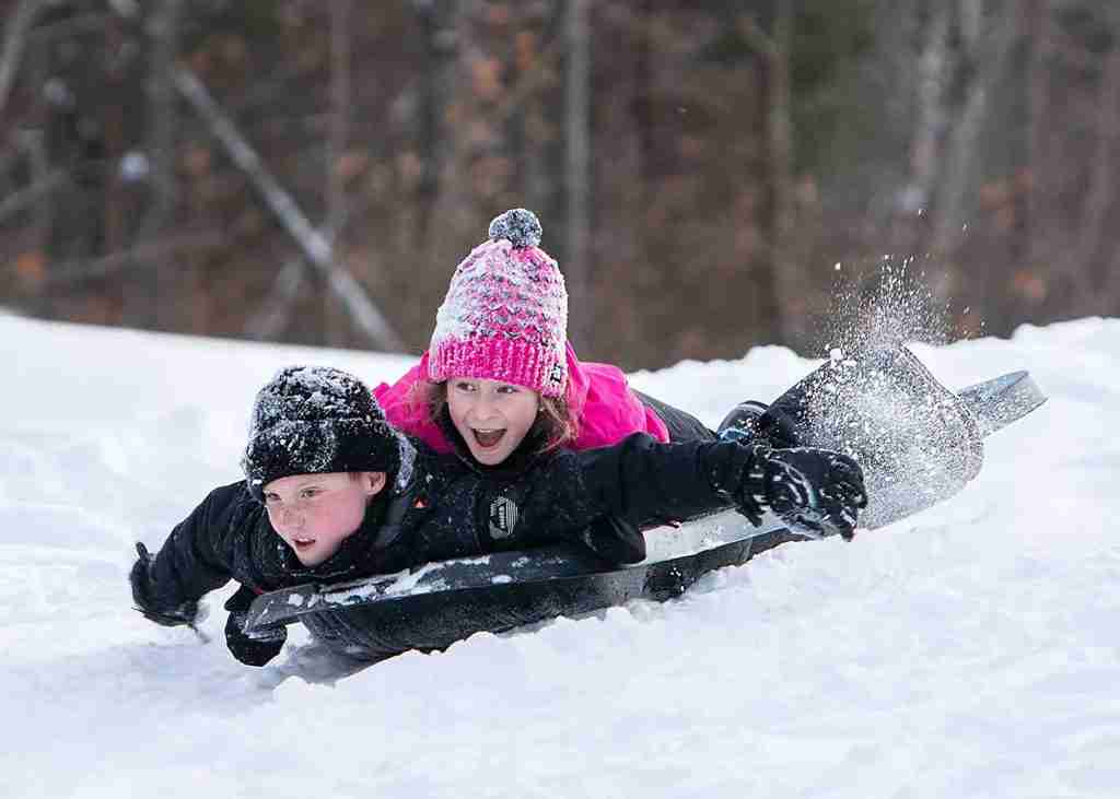 Two children having fun sledding down a snowy slope in a multi-seat Pelican Mega Utility Glider sled!