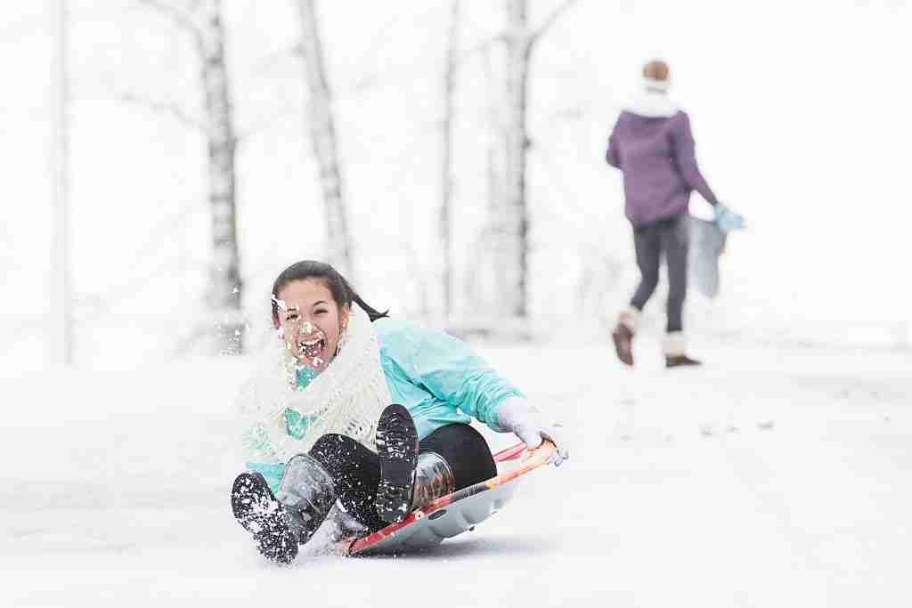 Young girls playing in the winter ice and snow, sliding down a hill on a sled.