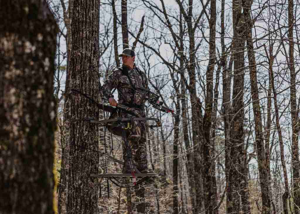 Man hunting on an elevated climbing tree stand in the woods
