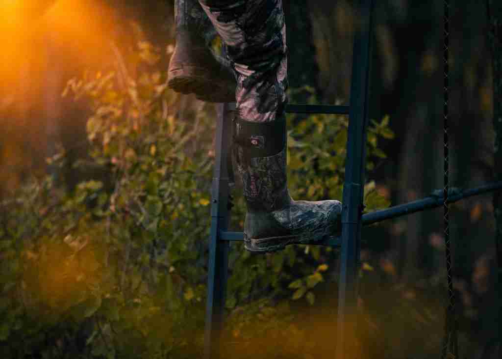 Closeup of boots as hunter climbs ladder tree stand in the woods at sunset golden hour