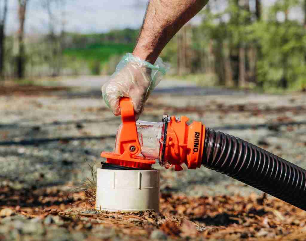 RV Sewer Adapter Pro pumping water from RV holding tank into inlet in the woods on a campsite.