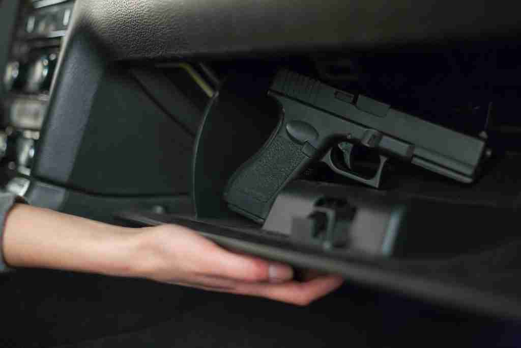 A hand holds one of the best portable gun safes with a handgun inside it.