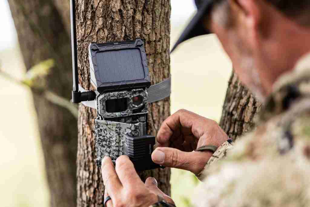 Man operating a trail camera strapped to a tree in the woods. 
