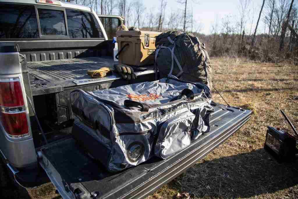 Camping gear sits in a truck bed outside in a wooded area. 