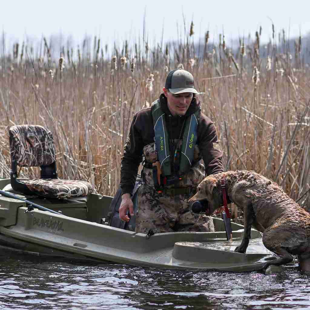 A hunter and a dog situated on a Beavertail Stealth Flip-Over Blind on a body of water