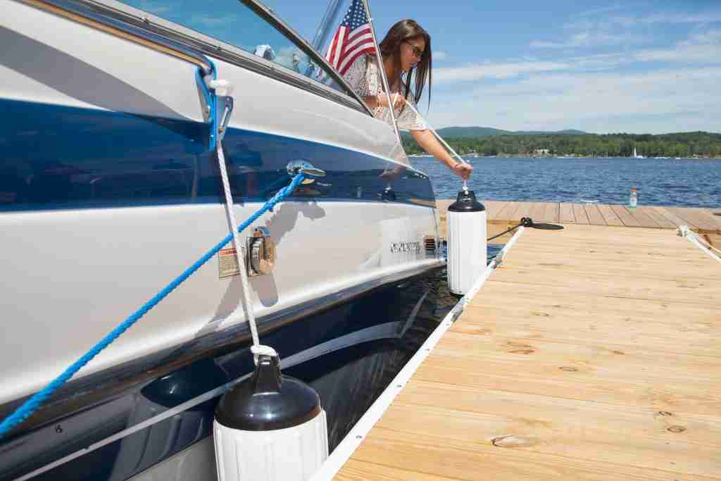 A woman hoists a boat fender over a boat between the boat and a dock