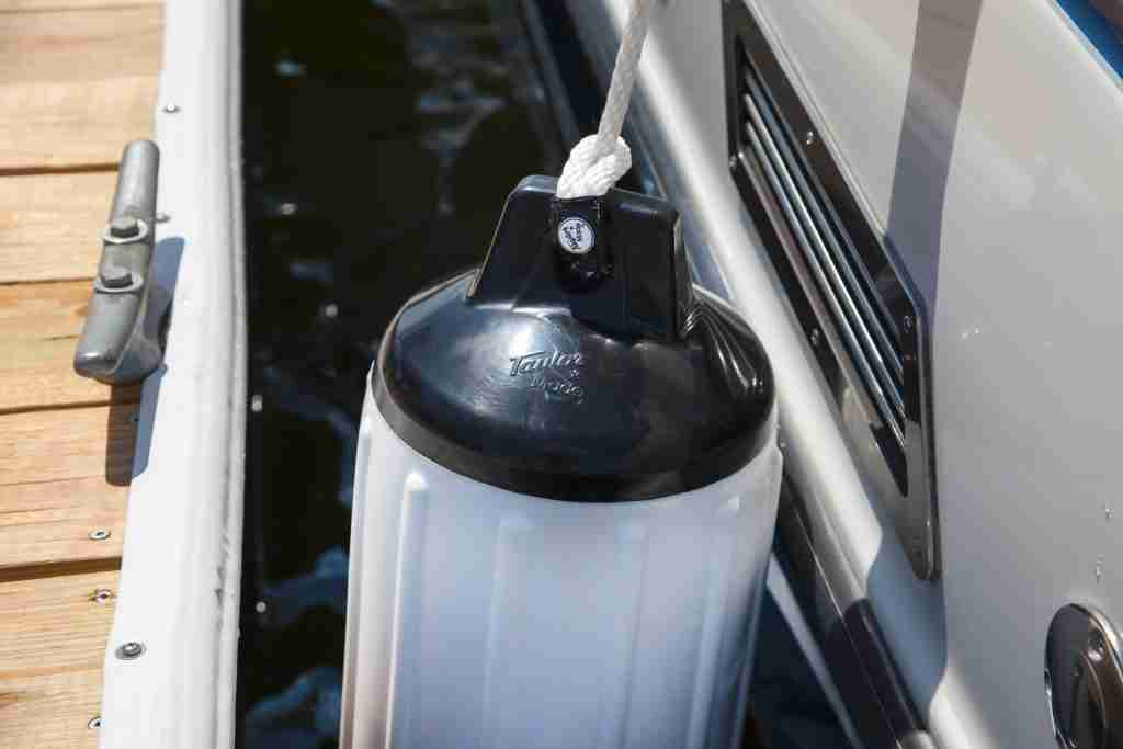 A white Taylor Made Boat Fender hangs from a boat on the water.