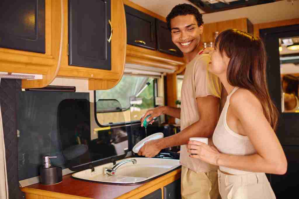 A man and woman stand in an RV kitchen smiling because they have air conditioning.