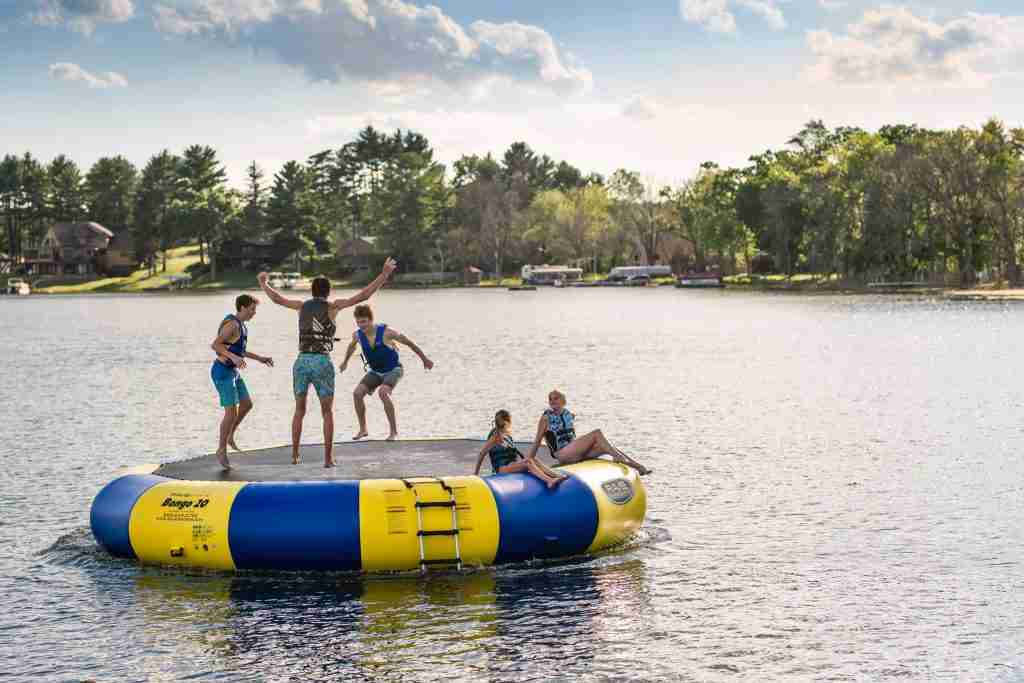 A group of people jump joyously on a floating trampoline on the lake. 