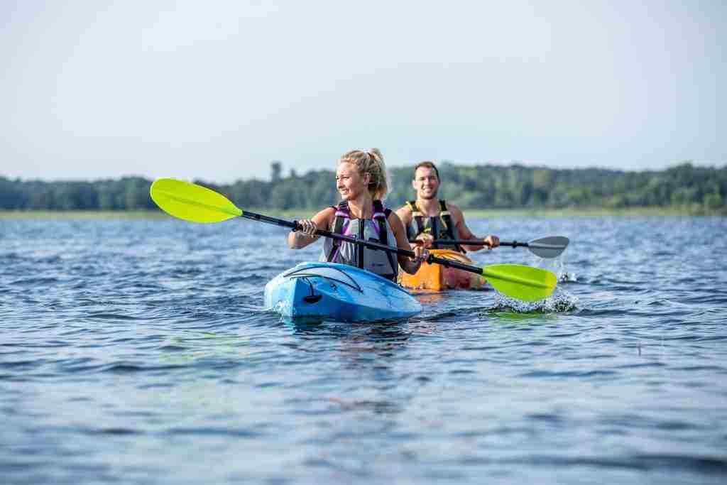 A woman and man paddle on kayaks in the ocean while wearing traditional life jackets and PFDs