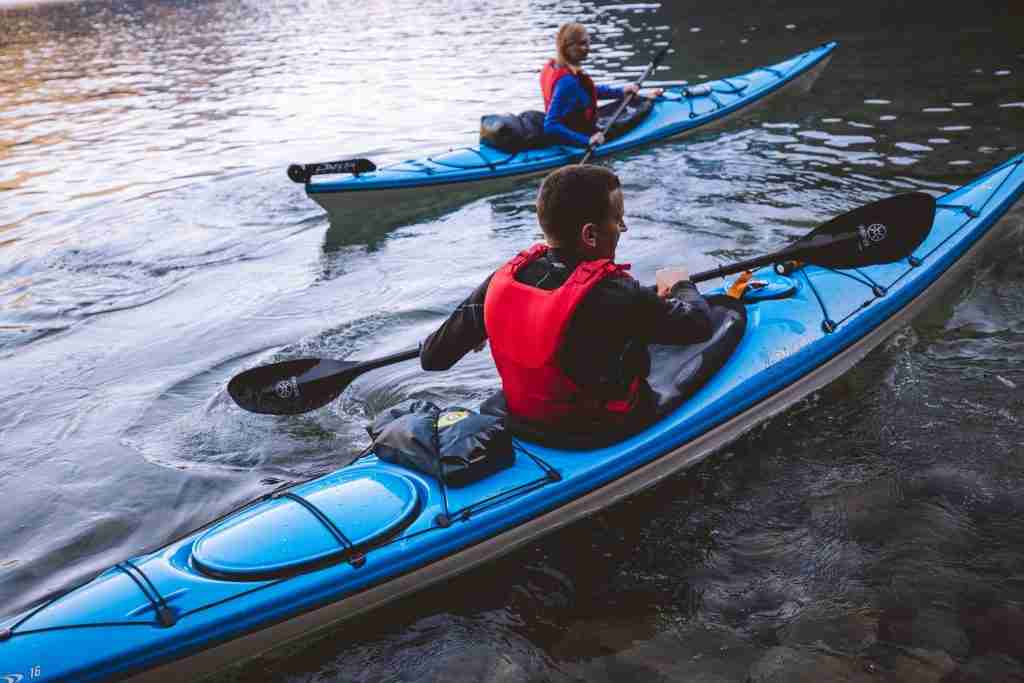 Two kayakers wearing orange life vests paddle on the water