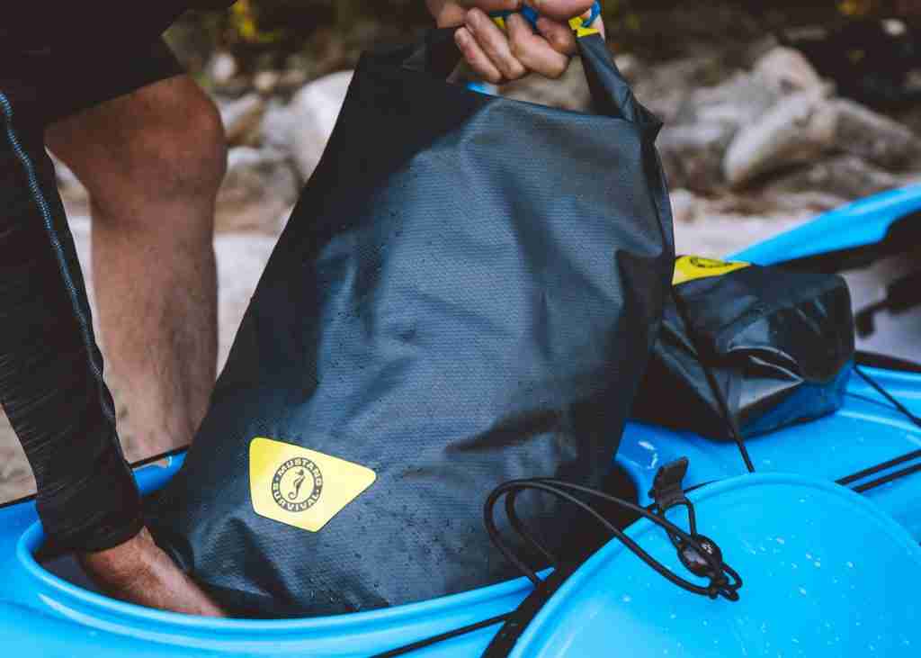 A man pulls a dry bag for holding kayak accessories out of a green kayak. 
